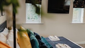 Una camera d'albergo con un letto, due finestre, una TV a schermo piatto e una pianta.