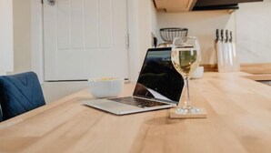 Un portatile su un tavolo di legno, con un bicchiere di vino bianco e una ciotola di cibo.