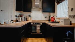 Una cucina compatta con mobili neri, forno integrato, macchina da caffè e contenitore per il pane.