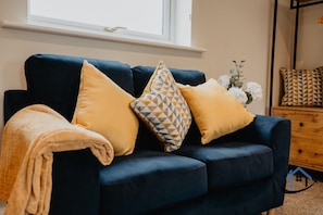 A dark blue sofa with three cushions, a wooden dresser, and a window with a view. - Shambles Retreat, studio, parkingx2 (Wiltshire)
