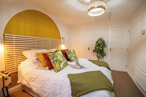 A bedroom with a bed, bedside lamps, a plant, and a door. - Ironside House 3 bed house, sleeps 8 parking (Thrapston)