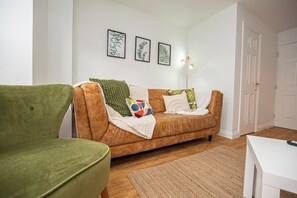 A living room with a brown sofa, a green armchair, and a white table. There are three framed pictures on the wall and a lamp on the right. - Ironside House 3 bed house, sleeps 8 parking (Thrapston)