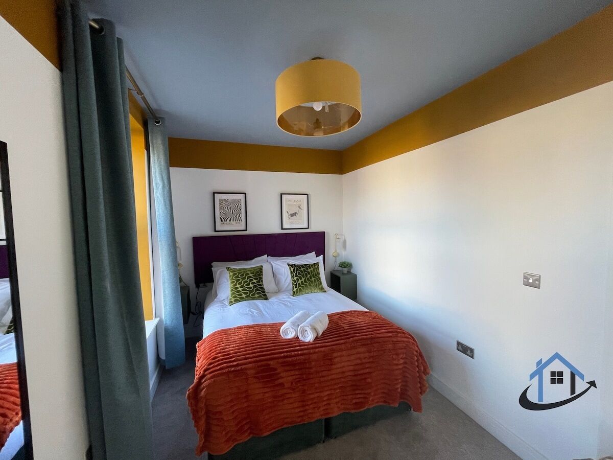 Quarto de hotel com cama, mesa de cabeceira, abajur e parede com um logotipo.