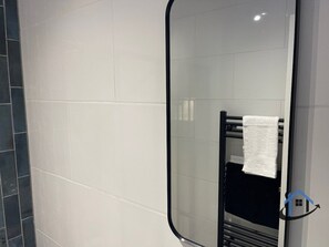 Ein Badezimmer mit weißen Fliesen, einem schwarzen Handtuchhalter und einem Spiegel.