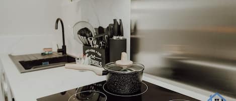 Una cocina con tope de inducción negro, una olla encima y un juego de utensilios de cocina al fondo.