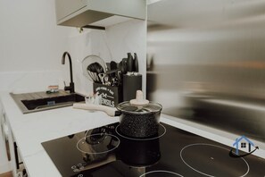A kitchen with a black induction cooktop, a pot on it, and a set of kitchen utensils in the background. - Apt 4 Manor House - 1 Bed 1 bath sleeps 2 parking (Desborough)