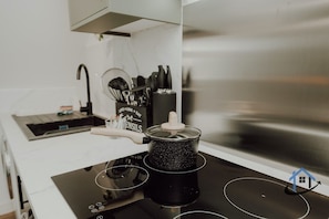 A kitchen with a black induction cooktop, a pot on it, and a set of kitchen utensils on the counter. - Penthouse - 5 bed 4 bath sleeps 10 parking wi-fi (Desborough)