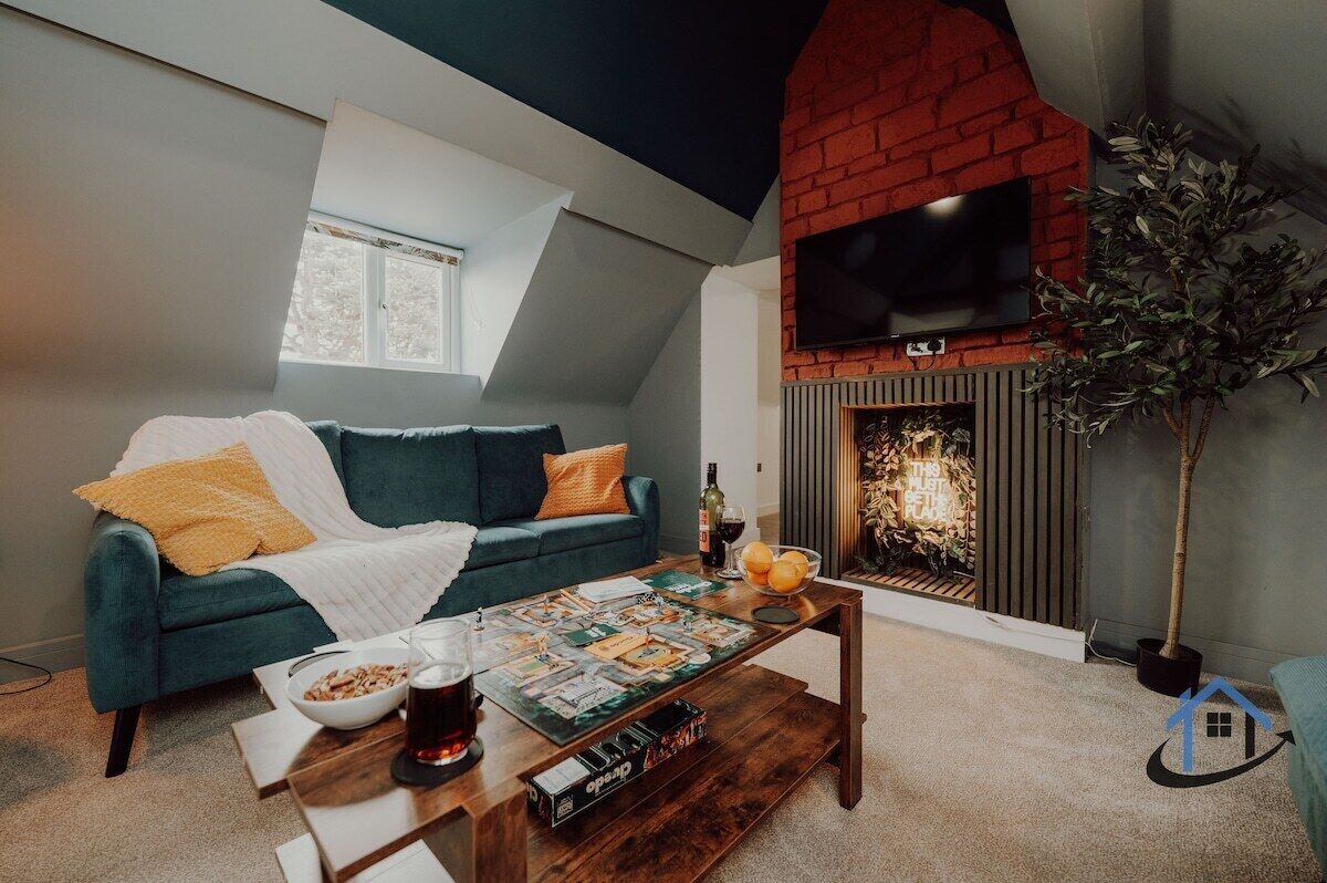 Een gezellige woonkamer met een open haard, een bank, een bijzettafeltje met gezelschapsspellen en een televisie boven de open haard.