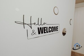 Una pared con un cartel que dice 'Hello & Welcome', un recorte circular y un logotipo con una casa y una flecha.