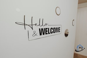 Eine Wand mit einem 'Hello & Welcome'-Schild, einer runden Aussparung und einem Logo mit einem Haus und einem Pfeil.
