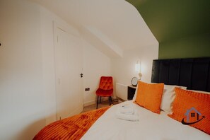 Een hotelkamer met een bed, een rode stoel, een nachtkastje met een lamp en een groene accentmuur.