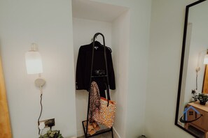 Ein Zimmer mit Kleiderhaken, einer aufhängenden Tasche, einer Lampe und einem Spiegel.