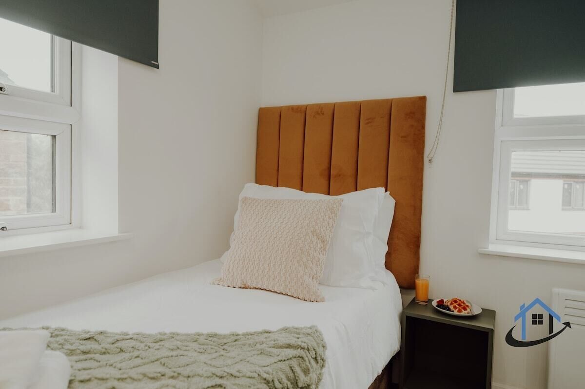 Uma cama de solteiro com cabeceira de madeira, roupa de cama branca e manta verde.
