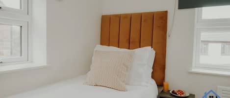 Una cama individual con cabecera de madera, ropa de cama blanca y una manta verde.
