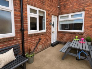 A brick exterior with two windows, a door, a bench, a table, and a potted plant. - Flat, sleeps 4, central, parking, Ground Floor (Bedlington)