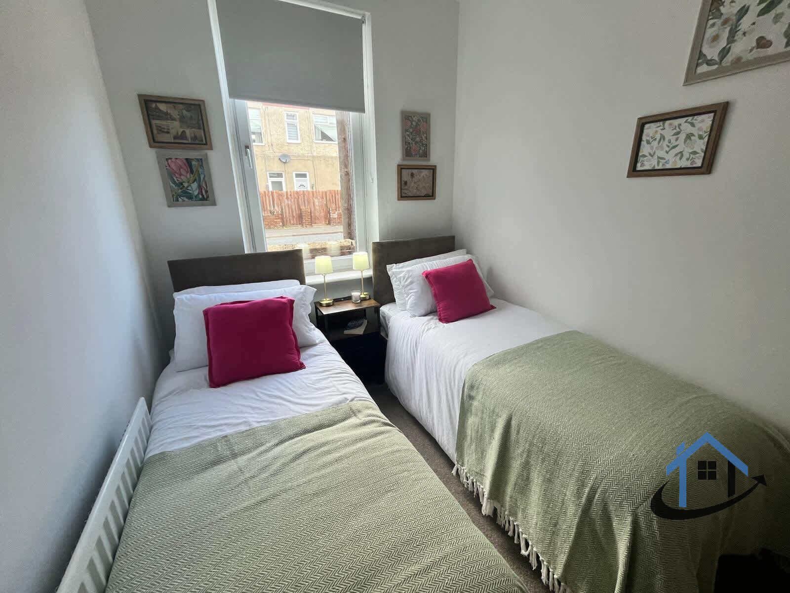 A bedroom with two single beds, a window, and a view of the outside.