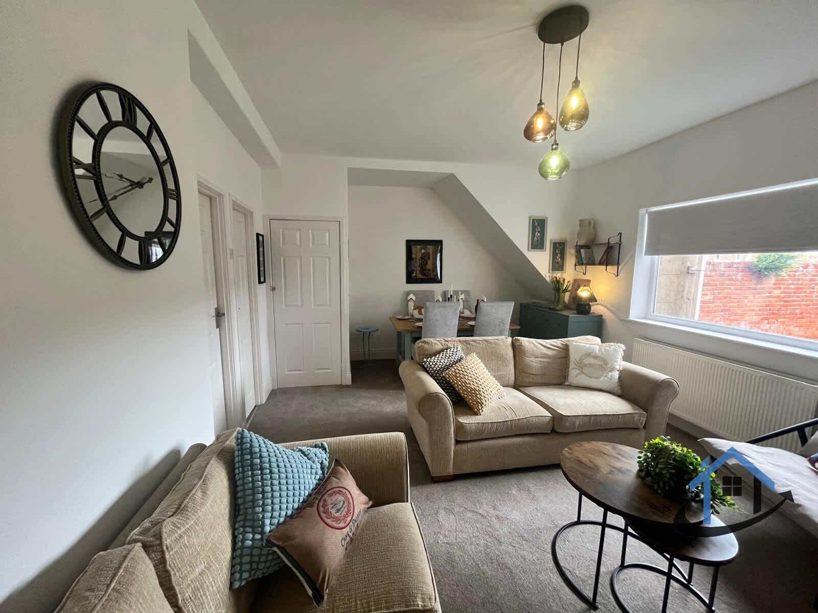 A living room with a sofa set, a coffee table, a clock on the wall, and a window with a view.