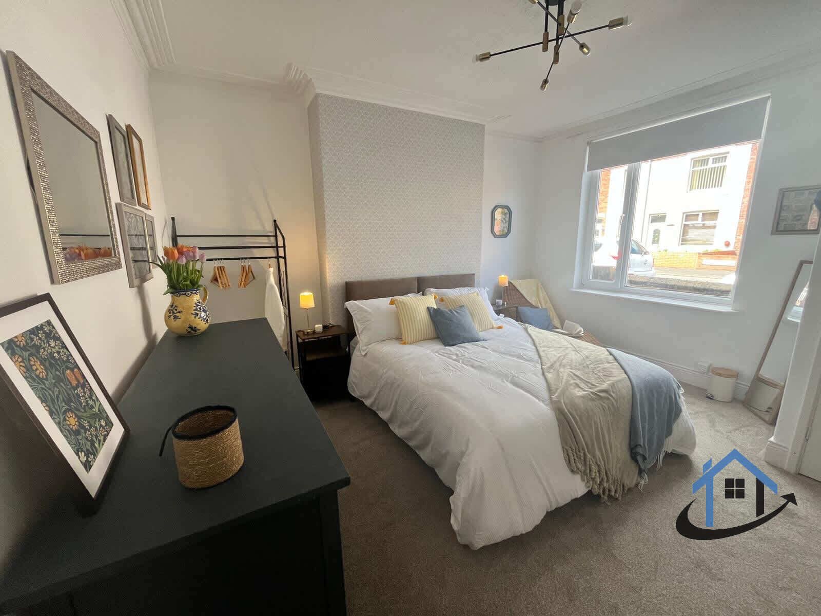Une chambre à coucher avec un lit, des tables de chevet, une lampe, une fenêtre et un miroir fixé au mur.