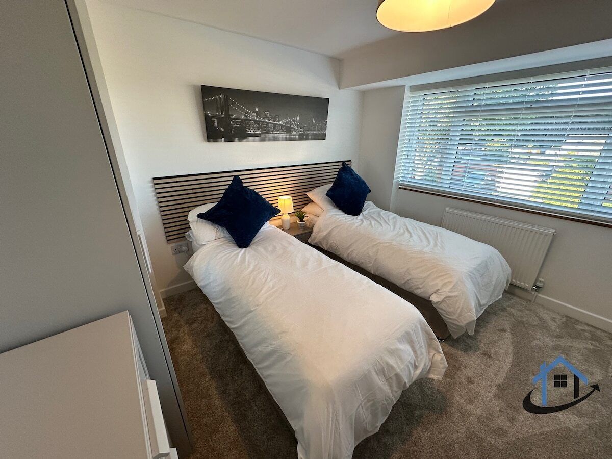 Un dormitorio con dos camas individuales, un radiador, una ventana con persianas y un cuadro con una vista urbana en la pared.