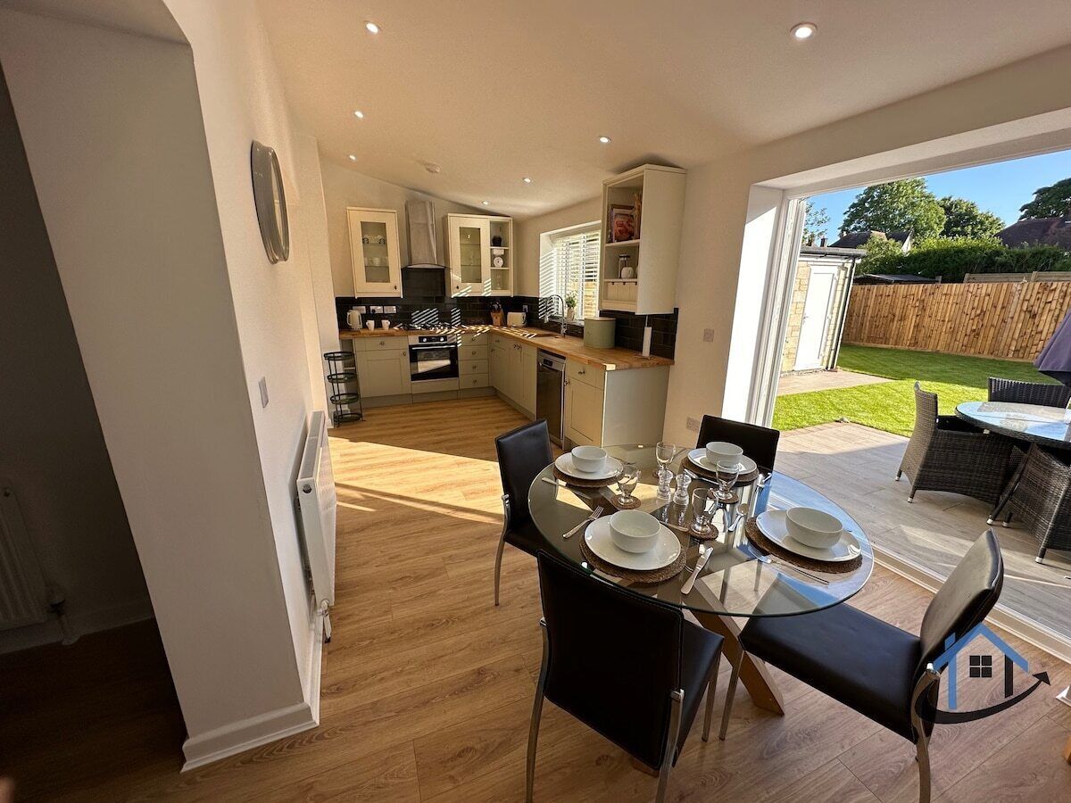 A modern kitchen with white cabinets, a dining area with a glass table, and a view of a backyard.