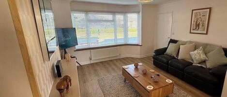 A living room with a wooden coffee table, a black sofa, and a window with blinds.