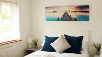 A bedroom with a bed, a nightstand, a lamp, a window, and a wall-mounted painting.