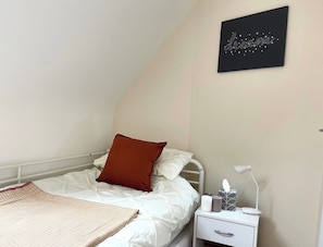 A bedroom with a bed, a nightstand, a lamp, and a wall-mounted artwork.