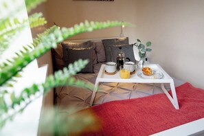 A cozy room with a bed, a white table with breakfast items, and a red throw blanket.