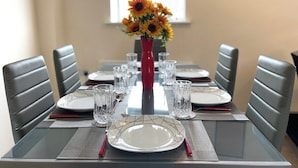 Mesa de comedor para seis personas, con un jarrón de girasoles, sillas tapizadas de color gris y una ventana al fondo.