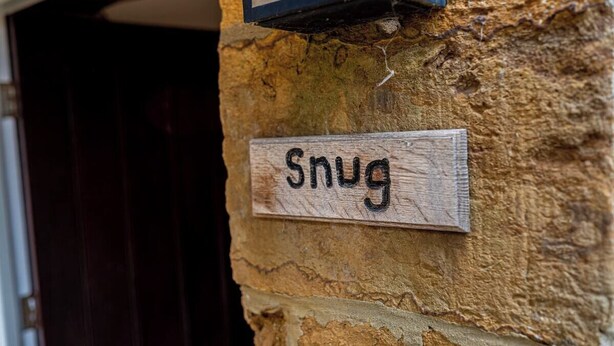 Uma placa de madeira com o nome 'Snug' fixada em uma parede de pedra texturizada.
