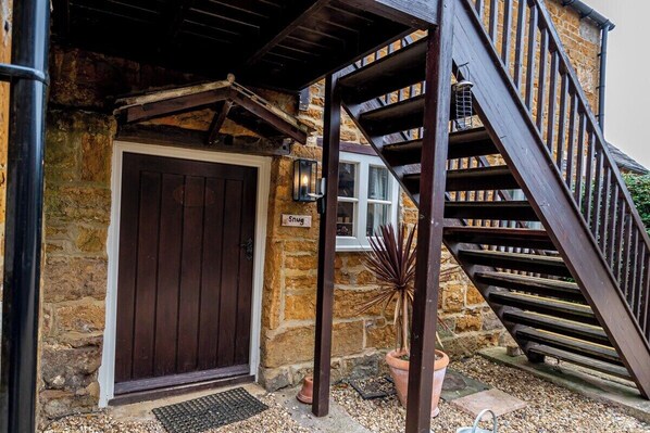 A stone building with a wooden staircase and a door labeled 'Snug.'