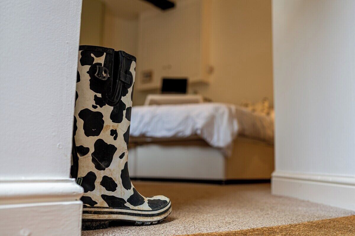 Ein Zimmer mit einem Bett, einem Nachttisch und einem Paar Stiefel, die an einer Wand lehnen.