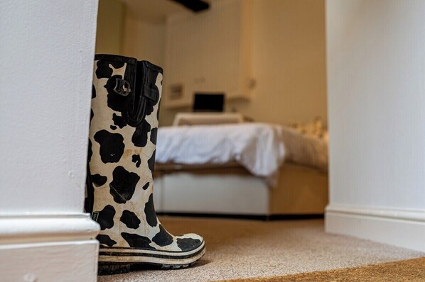 A room with a bed, a bedside table, and a pair of boots leaning against a wall.