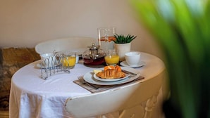 Mesa de café da manhã com um croissant, suco de laranja e uma cafeteira.