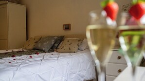 Quarto com cama, almofadas, mesa de cabeceira e um copo de vinho branco com morangos.