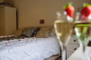 Ein Schlafzimmer mit einem Bett, Kissen, einem Nachttisch und einem Glas Weißwein mit Erdbeeren.