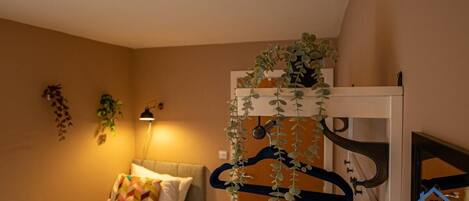 A bedroom with a bed, bedside table, lamp, and a wall-mounted plant.