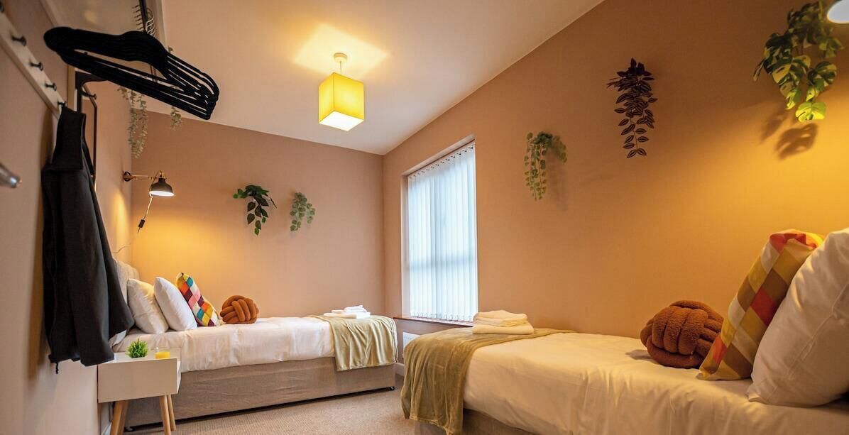Ein Schlafzimmer mit zwei Betten, einem Nachttisch, einem Kleiderständer, einer Lampe und einem Fenster mit Jalousien.