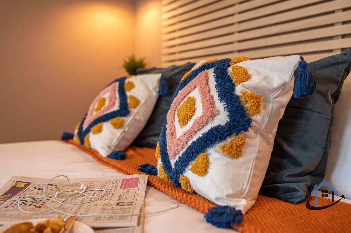 Un letto con due cuscini a motivo geometrico, una coppia di cuffie e un giornale.