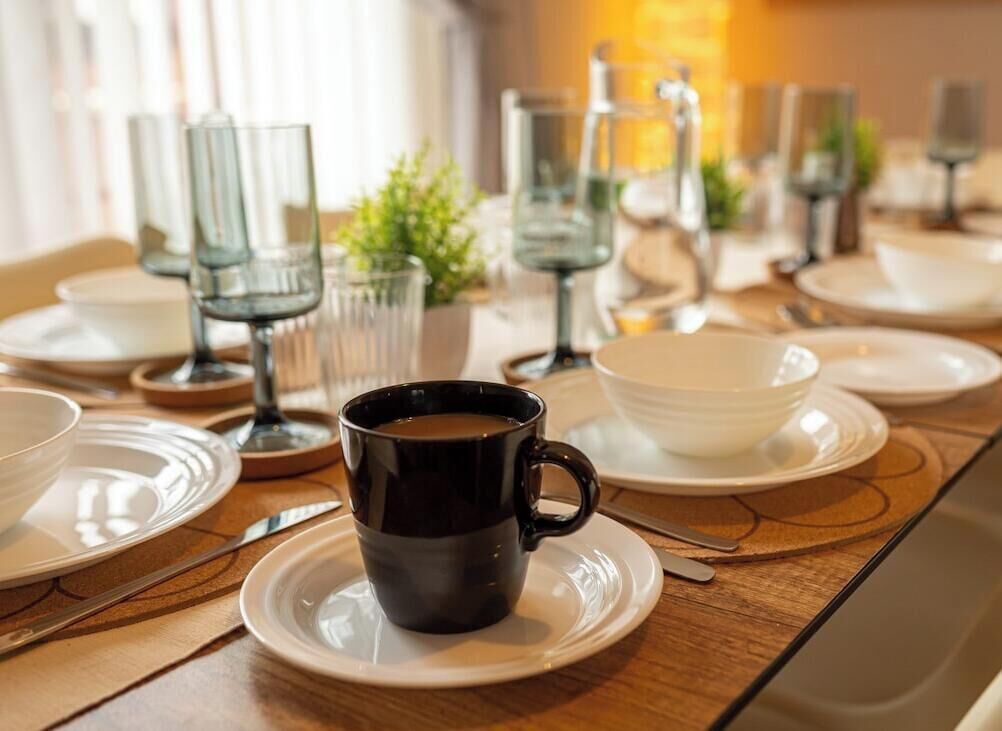 Une table à manger dressée avec des assiettes, une tasse noire et des verres transparents.