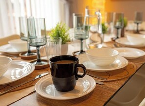 A dining table set with plates, a black cup, and clear glasses. - Minchin House 3 bed parking sleeps 8 (Northamptonshire)