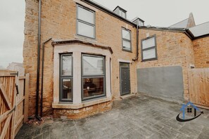 A corner of a brick house with a bay window, a door, and a garage door. - Apt 6 Manor House 1 Bed 1 bath sleeps 2 parking (Desborough)