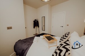 A bedroom with a bed, a bedside table, a mirror, a door, and a wall socket. - Apt 6 Manor House 1 Bed 1 bath sleeps 2 parking (Desborough)