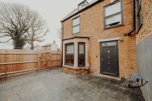 A two-story brick house with a corner bay window, a front door, and a wooden fence. - Apt 6 Manor House 1 Bed 1 bath sleeps 2 parking (Desborough)