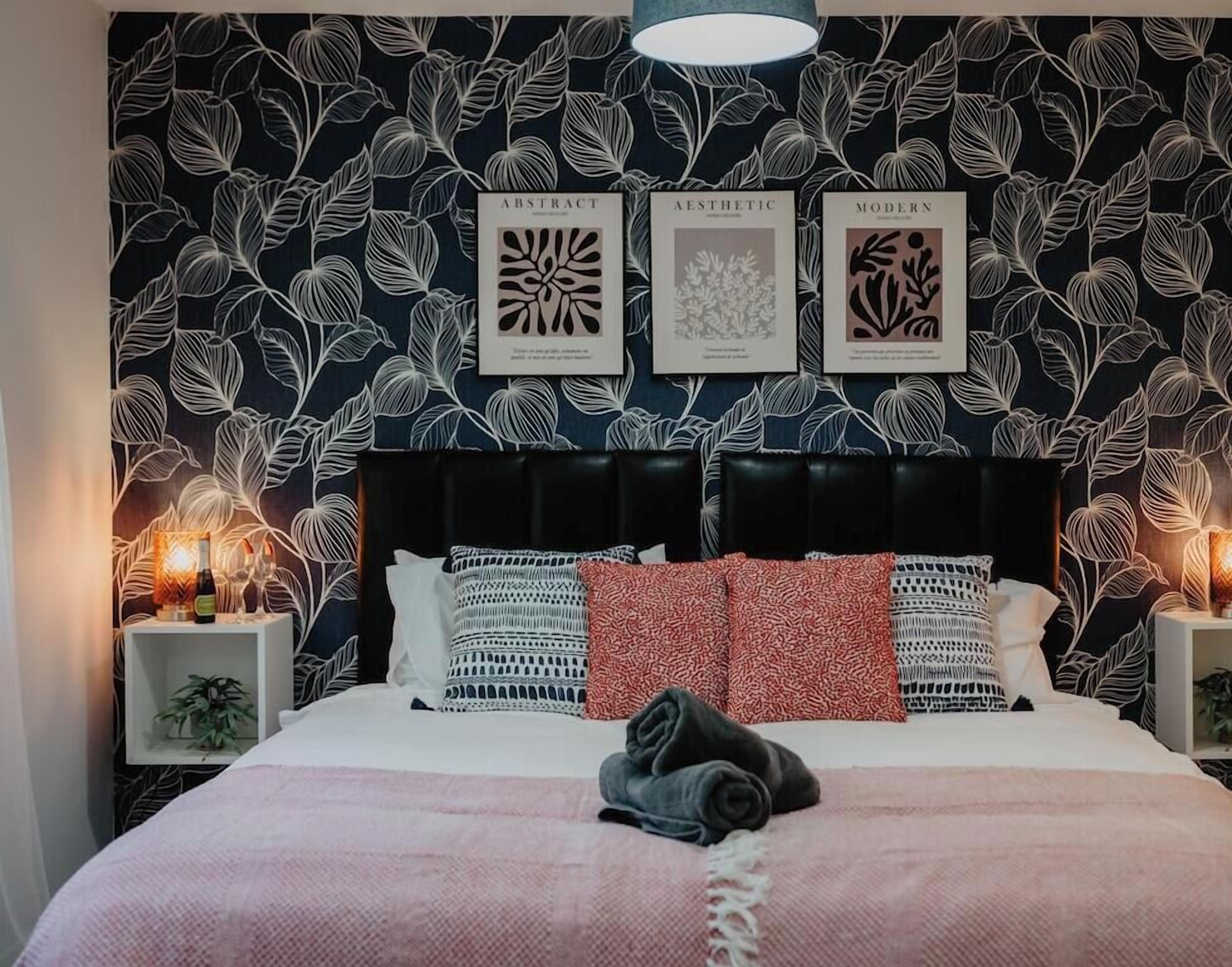 A bedroom with a patterned wallpaper, a black headboard, and a bedside lamp.
