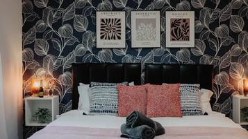 A bedroom with a patterned wallpaper, a black headboard, and a bedside lamp.