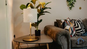 Ett modernt vardagsrum med ett runt bord, en golvlampa, en krukväxt och en soffa med mönstrade kuddar.