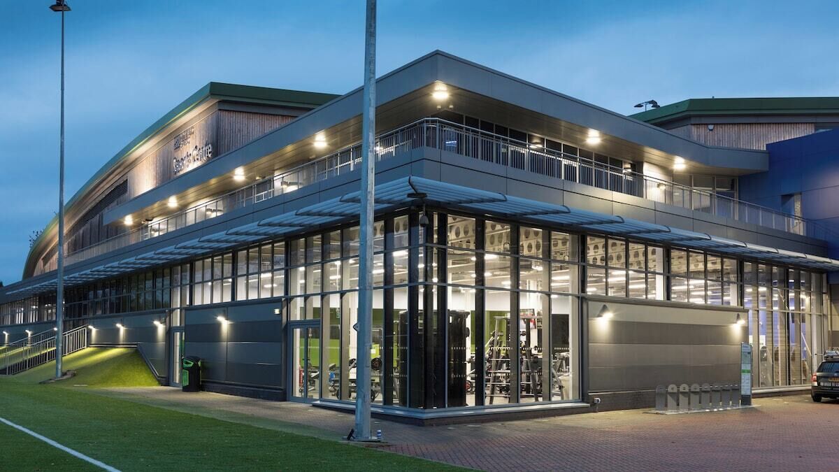 Un bâtiment moderne doté d’une façade en verre, d’un espace extérieur aménagé pour s’asseoir et d’une entrée couverte.