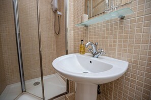 A bathroom with a white sink, a glass shower enclosure, and a glass shelf above the sink.
