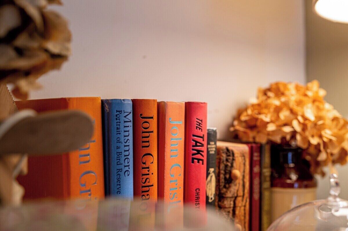 Une rangée de livres sur une étagère, avec un vase de fleurs séchées en arrière-plan.